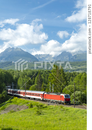 Passenger train passing through the green valley of Strba in Slovakia with the High Tatras Mountains in the background 128718791