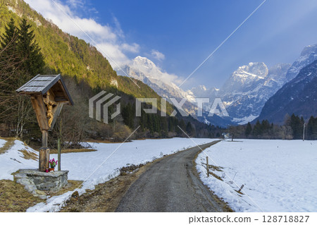 Wooden wayside cross overlooking snowy Log pod Mangartom valley in Slovenia Wooden wayside cross overlooking snowy Log pod Mangartom valley in Slovenia 128718827