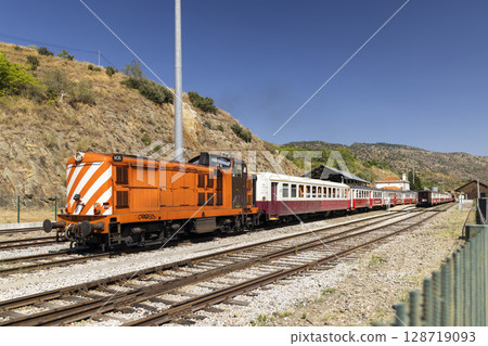 Orange diesel locomotive pulling passenger train in Carrazeda de Ansiaes, Portugal Orange diesel locomotive pulling passenger train in Carrazeda de Ansiaes, Portugal 128719093