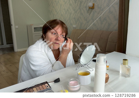 A graceful senior lady is seated at her home, preparing her look for the day. 128719286