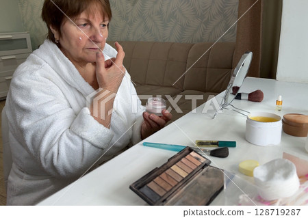 An elegant elderly lady is relaxing at her house, applying her makeup for the day. 128719287