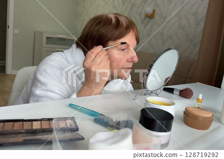 An older woman with charm is sitting in her living room, doing her makeup routine. 128719292