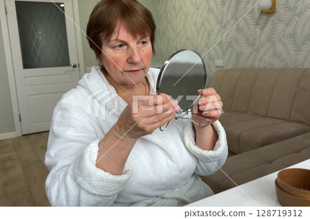 A refined senior lady is at her residence, carefully applying her makeup. A refined senior lady is at her residence, carefully applying her makeup. 128719312