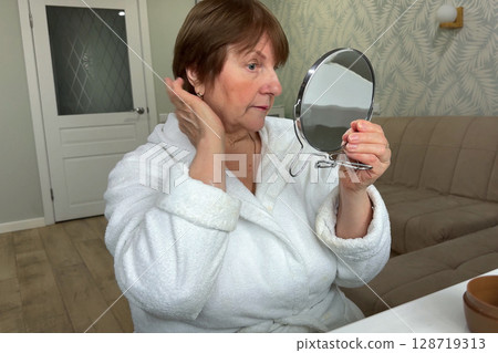 A refined senior lady is at her residence, carefully applying her makeup. A refined senior lady is at her residence, carefully applying her makeup. 128719313