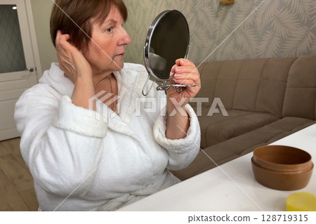 A refined senior lady is at her residence, carefully applying her makeup. 128719315