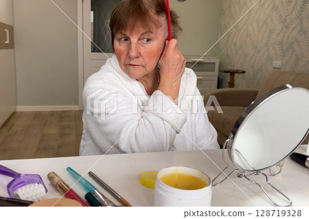 A sophisticated senior woman is at home, focusing on her morning grooming. 128719328