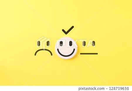 Customer Satisfaction Feedback Choice Concept. Smile face on wooden block selected among sad and neutral faces, symbolizing customer satisfaction, review ratings, and positive feedback in surveys. 128719638