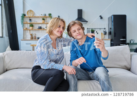 Middle aged mother and teenage son sitting together at home taking selfie photo on smartphone 128719786