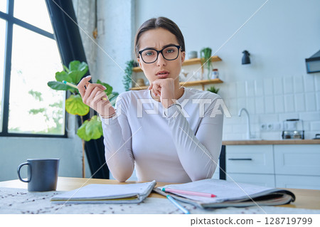 Webcam portrait serious female student teenager, sitting at home at the table Webcam portrait serious female student teenager, sitting at home at the table 128719799