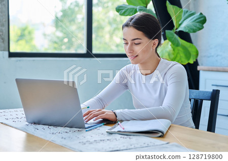 Teenage girl student sitting at the table with laptop, textbooks in home interior Teenage girl student sitting at the table with laptop, textbooks in home interior 128719800