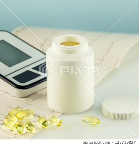 Mockup of natural vitamins or supplements, cardiogram and tonometer on doctor desk. White bottle with healthy supplements in gel capsules. Omega 3. Vitamins and nutrients for heart 128719827