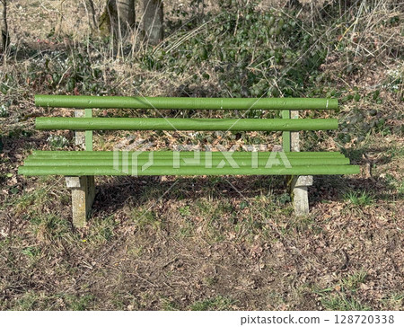 Green wooden bench in sunny park. Public space, relaxation area, and outdoor urban furniture 128720338