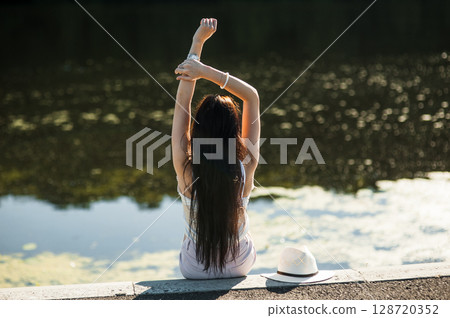 A girl sits on the shore of a lake 128720352