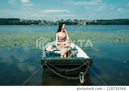 A young girl is sitting in a boat on the lake 128720368