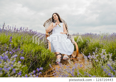 In the middle of the lavender field, there is a rocking chair where a young woman sits 128720443