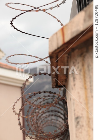 Razor wire coils create a formidable barrier along the edge of a concrete wall, enhancing security while contrasting with the cloudy sky in the background Razor wire coils create a formidable barrier along the edge of a concrete wall, enhancing security while contrasting with the cloudy sky in the background 128720499