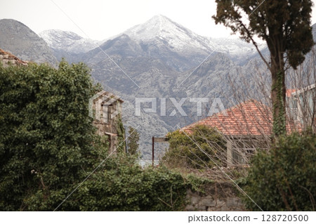 Snow capped mountains rise behind rustic buildings in a serene village landscape during a winter day in the countryside Snow capped mountains rise behind rustic buildings in a serene village landscape during a winter day in the countryside 128720500