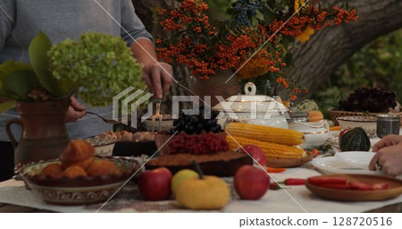 Thanksgiving dinner celebration with festive table settings featuring seasonal harvest, vibrant flowers, assorted dishes, and warm ambiance created by family gathering outdoors 128720516