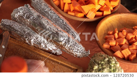Delicious corn wrapped in foil sits next to vibrant orange pumpkin pieces ready for cooking, capturing the essence of autumn flavors and seasonal ingredients preparation Delicious corn wrapped in foil sits next to vibrant orange pumpkin pieces ready for cooking, capturing the essence of autumn flavors and seasonal ingredients preparation 128720530