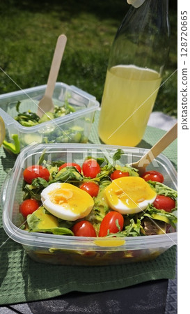 Fresh tuna salad with cherry tomatoes, arugula and soft-boiled egg in plastic container on picnic table. Concept of healthy eating, outdoor lunch and nutritious summer lifestyle Fresh tuna salad with cherry tomatoes, arugula and soft-boiled egg in plastic container on picnic table. Concept of healthy eating, outdoor lunch and nutritious summer lifestyle 128720665