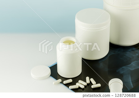 Mockup of supplements for skin, bones and joints. Calcium Ca supplements for Bone human health. Bone and joint health. White bottles with capsules and X-ray film on doctor desk. Copy space Mockup of supplements for skin, bones and joints. Calcium Ca supplements for Bone human health. Bone and joint health. White bottles with capsules and X-ray film on doctor desk. Copy space 128720688
