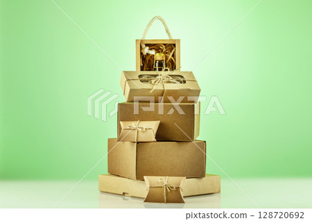 Eco friendly holiday shopping and delivery. Craft cardboard gift boxes with wooden box with bottle of champagne in form new year tree on green gradient background. Christmas and New Year shopping Eco friendly holiday shopping and delivery. Craft cardboard gift boxes with wooden box with bottle of champagne in form new year tree on green gradient background. Christmas and New Year shopping 128720692