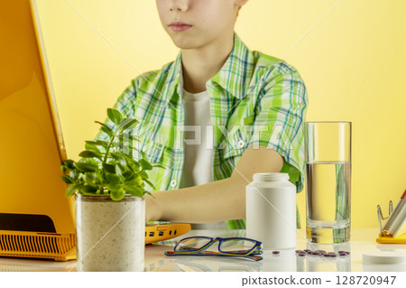 Boy using laptop, studies online at home and washes down vitamins in gel capsules with water. Supplements of Omega 3 or D 3 are good for kid health. Mockup of natural kid vitamins or supplements Boy using laptop, studies online at home and washes down vitamins in gel capsules with water. Supplements of Omega 3 or D 3 are good for kid health. Mockup of natural kid vitamins or supplements 128720947