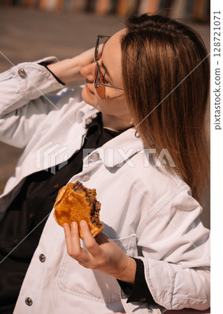 Enjoying a delicious burger while relaxing outdoors in stylish casual attire 128721071