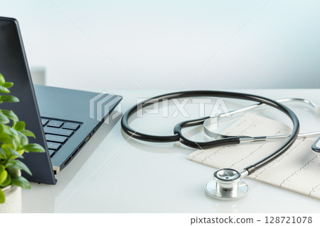 Doctor's office desk with laptop, medical documents, cardiogram, tonometer and stethoscope on a blue background. Medicine, medication treatment and medical examination concept 128721078