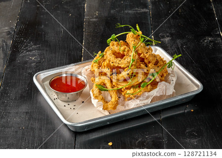 Deep fried onion rings with spicy sauce and pea sprouts on metal tray 128721134