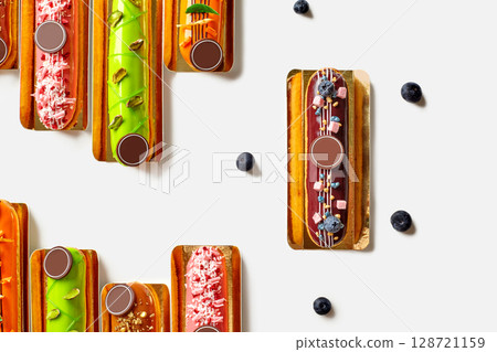 Colorful eclairs with creative toppings forming a pattern on white background 128721159
