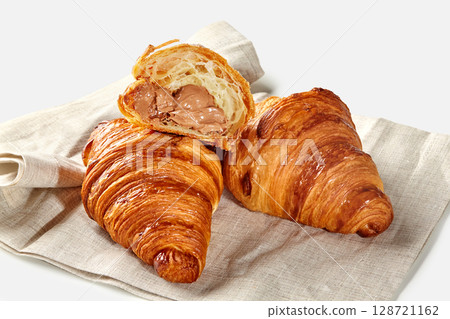 Delicious croissants with chocolate cream filling resting on linen napkin 128721162