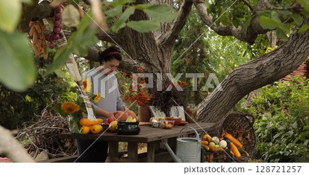 Rustic garden retreat with woman preparing seasonal produce surrounded by vibrant flowers and natural elements during warm afternoon light 128721257