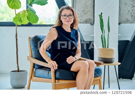 Portrait of middle aged business woman in black dress sitting in chair 128721506