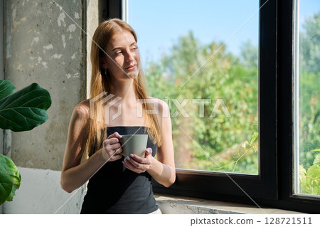 Portrait of smiling dreamy young woman with cup, profile view near window Portrait of smiling dreamy young woman with cup, profile view near window 128721511