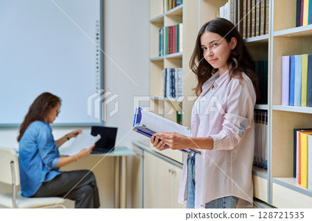 Portrait of teenage beautiful girl high school student with book in library classroom Portrait of teenage beautiful girl high school student with book in library classroom 128721535