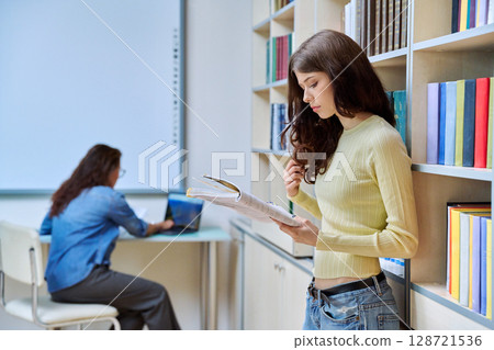 Portrait of teenage beautiful girl high school student reading textbook in library classroom 128721536
