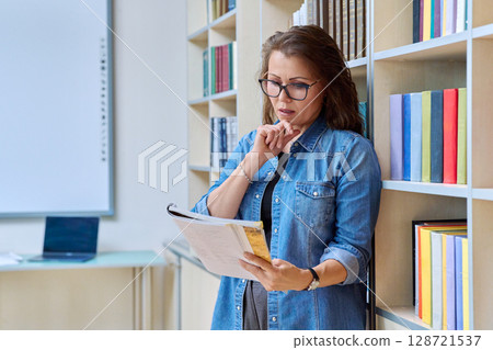 Portrait serious mature woman teacher, educational specialist reading textbook in classroom Portrait serious mature woman teacher, educational specialist reading textbook in classroom 128721537
