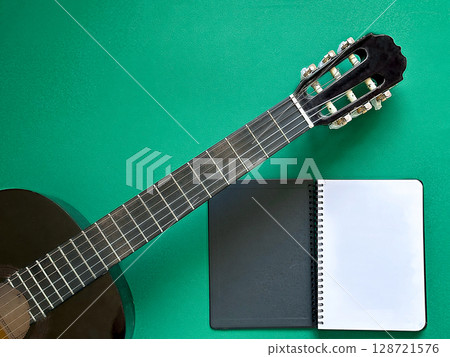 A close-up of a classical guitar and a blank notebook on a green background.  128721576