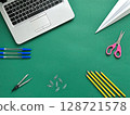 A textured green background with school supplies. Includes a laptop, scissors, yellow pencils, paper clips, and blue pens  128721578