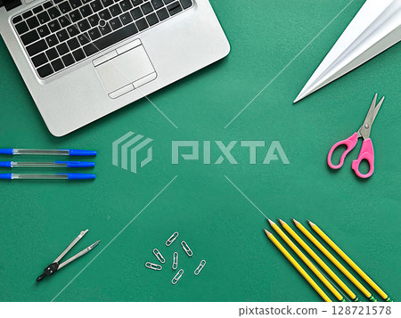 A textured green background with school supplies. Includes a laptop, scissors, yellow pencils, paper clips, and blue pens  128721578