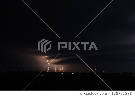 Night scene with multiple lightning bolts striking from dark storm clouds. 128721588