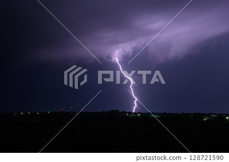 Single powerful lightning bolt hitting the ground from storm clouds at night. 128721590