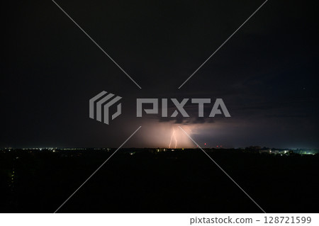 Lightning bolts and storm clouds over city during night. 128721599