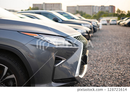 A row of cars are parked outdoors, with a focus on the front of a gray luxury SUV. The image highlights the sleek design and modern aesthetic of the vehicles. 128721614