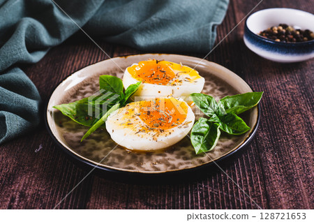 Soft-boiled egg split in half with spices and basil leaves on a plate on a table Soft-boiled egg split in half with spices and basil leaves on a plate on a table 128721653