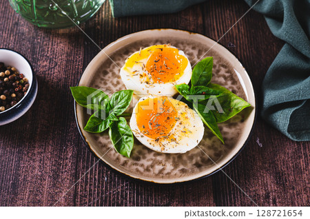 Spicy soft-boiled egg halves and basil on a plate on a table Spicy soft-boiled egg halves and basil on a plate on a table 128721654