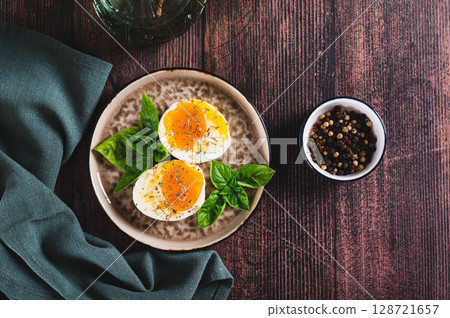 Soft-boiled egg split in half with spices and basil leaves on a plate on a table top view 128721657