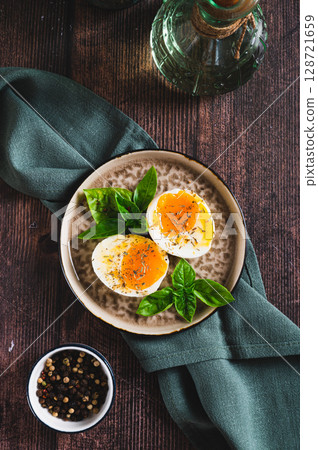 Spicy soft-boiled egg halves and basil on a plate on a table top and vertical view Spicy soft-boiled egg halves and basil on a plate on a table top and vertical view 128721659