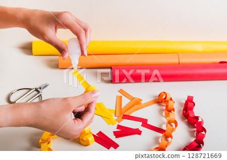 A girl's hands pour glue onto a strip of paper to make a paper chain A girl's hands pour glue onto a strip of paper to make a paper chain 128721669